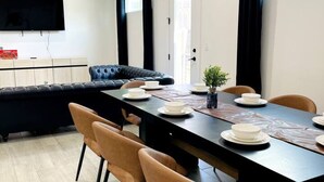 A modern dining area with a long table, six chairs, and a black sofa.