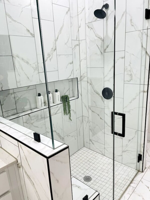 A modern bathroom with a glass shower enclosure, marble walls, and a mirrored vanity.