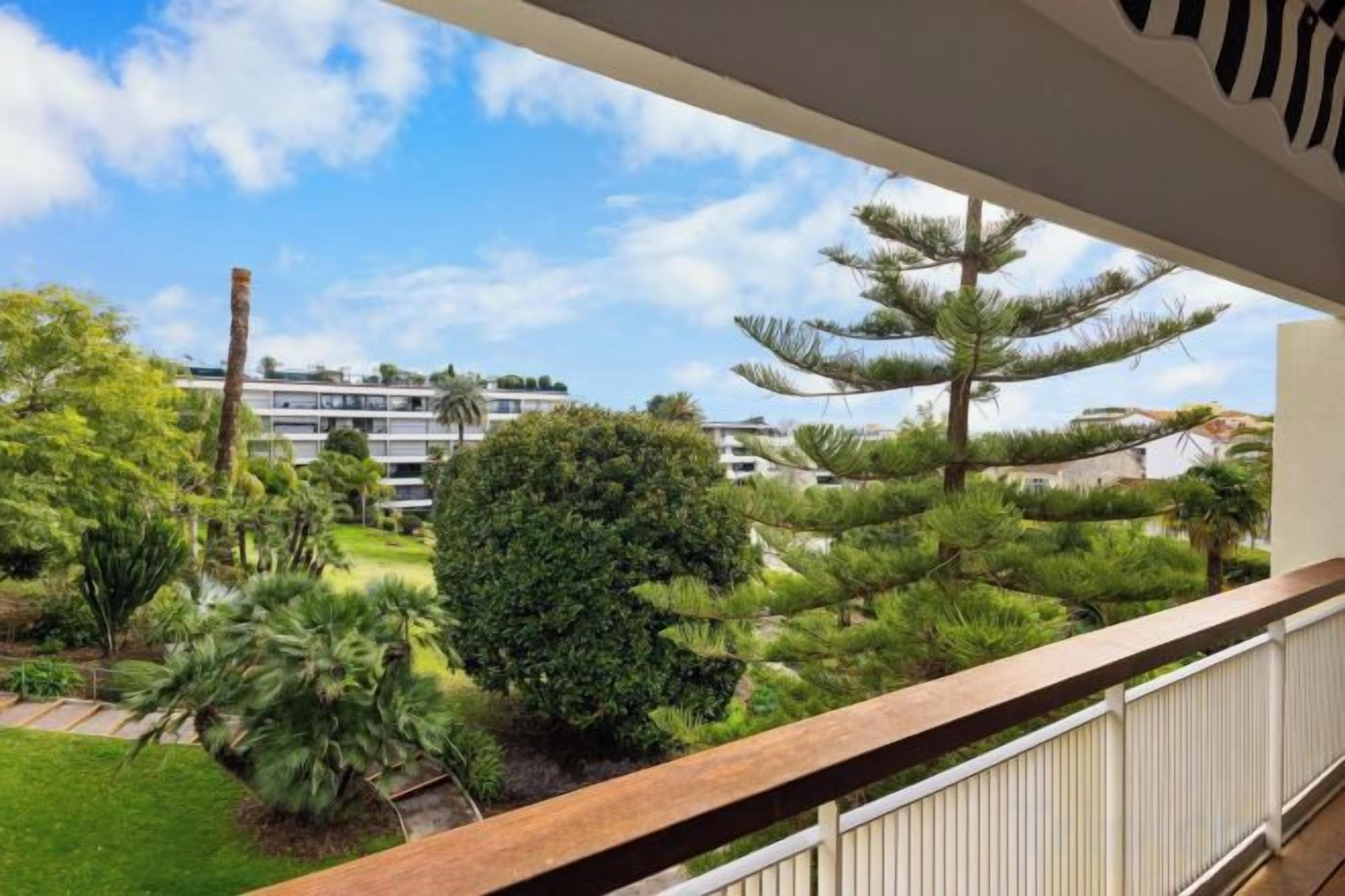 A balcony with a view of a landscaped garden and a building in the background.