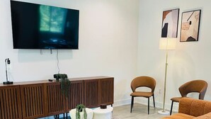 Un salon moderne avec un grand téléviseur à écran plat fixé au mur, une console en bois, deux fauteuils marron, un grand canapé orange et un lampadaire.