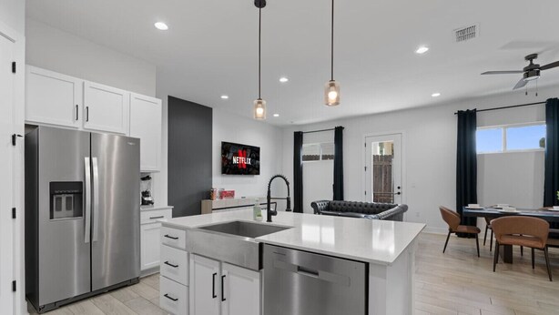 A modern kitchen with stainless steel appliances, a central island, pendant lighting, and a dining area with a leather couch. - Mega Lux Combined Unit - Up to 36 Guests (Austin)