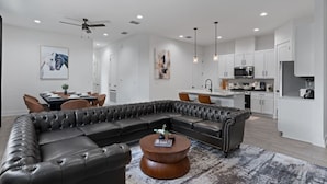 A modern living room with a sectional sofa, a dining area, and a kitchen with white cabinets and stainless steel appliances. - Mega Lux Combined Unit - Up to 36 Guests (Austin)