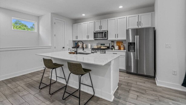 A modern kitchen with white cabinetry, a stainless steel refrigerator, a microwave, and a large island with two bar stools. - Stylish Retreat - Close to Downtown - Open Layout (Austin)