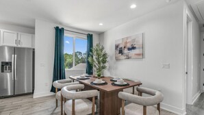 A modern kitchen with a stainless steel refrigerator, a dining area with a wooden table and four chairs, a potted plant, and a painting on the wall. - Stylish Retreat - Close to Downtown - Open Layout (Austin)
