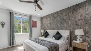 A bedroom with a bed, a ceiling fan, a window with curtains, a nightstand with a lamp, and a textured wall. - Stylish Retreat - Close to Downtown - Open Layout (Austin)