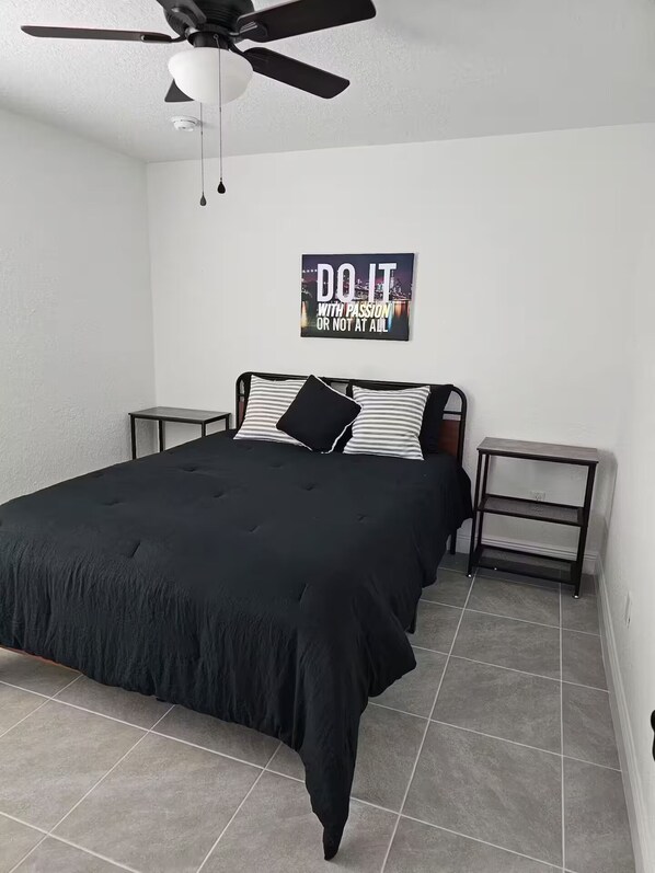 A bedroom with a bed, a ceiling fan, a motivational poster, and a nightstand.