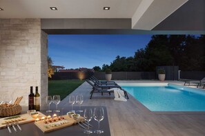 Un área de piscina al aire libre con sillones de descanso, una mesa de comedor preparada con comida y bebidas, y una pared de piedra.