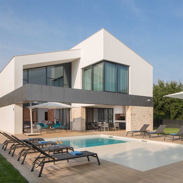 Una casa moderna de dos pisos con piscina, mobiliario exterior y fachada de piedra.