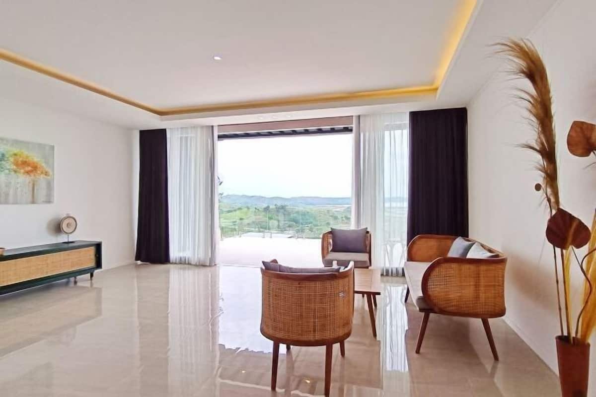 A spacious room with a large window, a sofa, two wicker chairs, a console table, and a decorative plant.