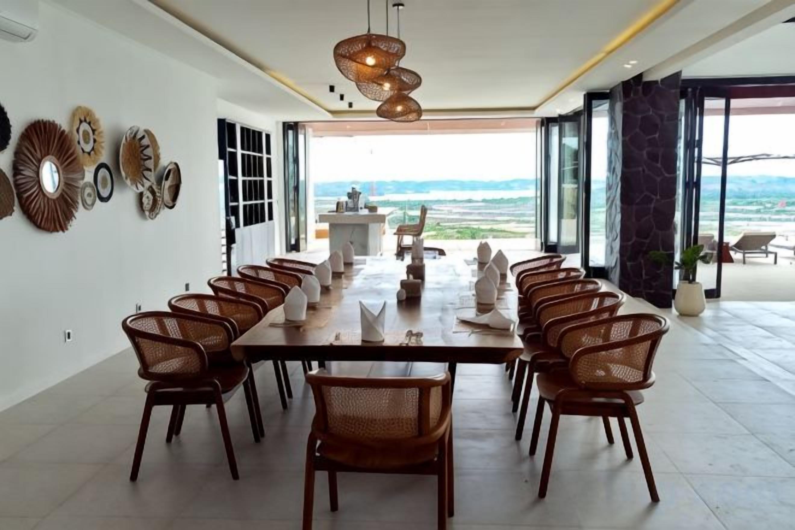 A dining area with a long table and chairs, a chandelier, and a view of the outdoors.