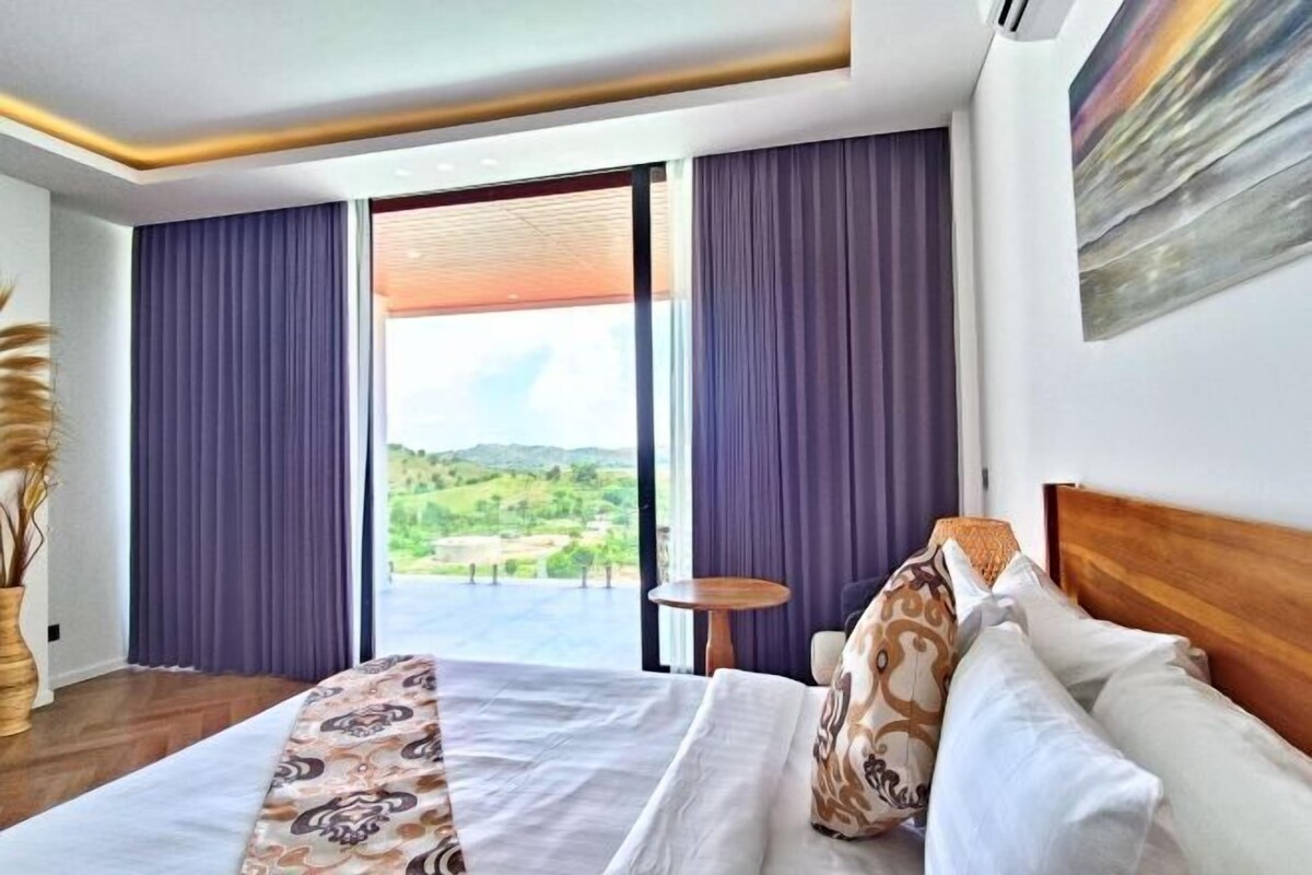 A hotel room with a large bed, a view of the countryside, and a small round table.