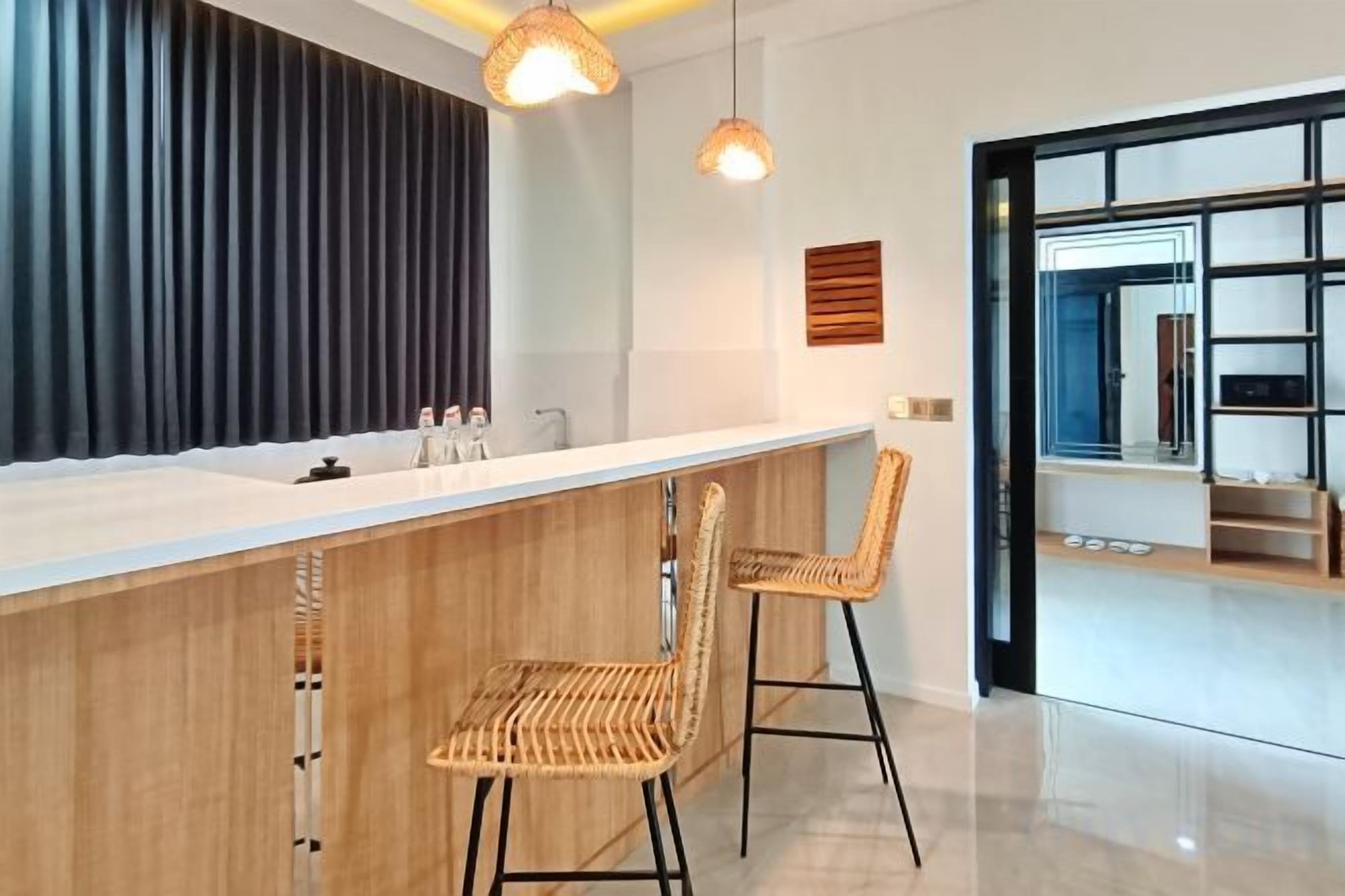 A modern kitchen with a white countertop, two wicker bar stools, and pendant lighting.