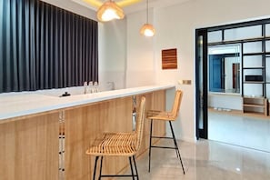 A modern kitchen with a white countertop, two wicker bar stools, and pendant lighting.