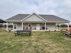 A single-story house with a covered porch, a barbecue grill, and a picnic table.