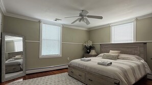 A bedroom with a bed, a ceiling fan, a mirror, and a window with blinds.