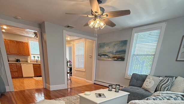 A living room with a gray sofa, a white coffee table, and a patterned rug. There is a ceiling fan and a painting on the wall.
