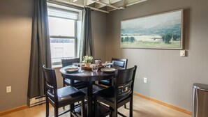 A dining area with a round table, four chairs, a painting of a landscape, and a window with curtains. - 5 mins to Downtown I King I Loft I Keyless Entry (Fargo)