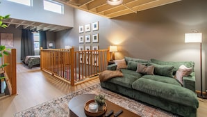 A spacious living area with a green sofa, wooden railing, and a patterned rug. - 5 mins to Downtown I King I Loft I Keyless Entry (Fargo)
