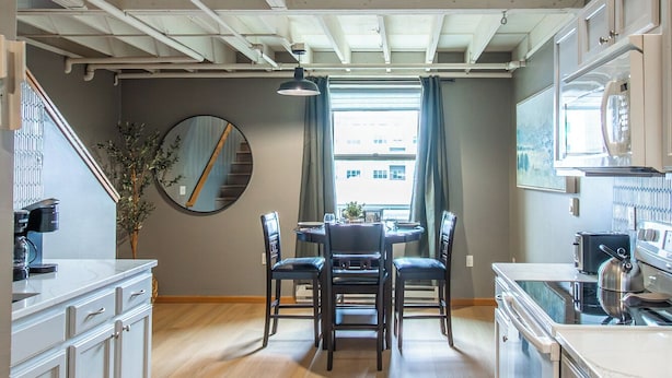 A modern kitchen with a dining area, wooden staircase, and a view of the city. - 5 mins to Downtown I King I Loft I Keyless Entry (Fargo)