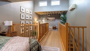 A spacious room with a wooden staircase, a bed with a green and white duvet, a small side table with a lamp, and a wall decorated with framed pictures. - 5 mins to Downtown I King I Loft I Keyless Entry (Fargo)