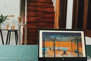 A laptop displaying a photo of a room with a wooden floor, a blue table, and a chair. - Venn Hostel (Vientiane)