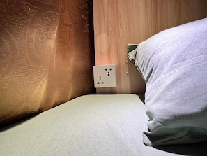 A bed with a white pillow and a power outlet on the wall. - Venn Hostel (Vientiane)