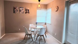 A dining area with a round table, four chairs, a vase with flowers, a wall clock, and a geometric light fixture. - Quiet & Private Greek-Inspired Coach House in Ladner (Delta)