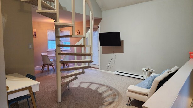 A room with a spiral staircase, a flat-screen TV mounted on the wall, a small round rug, and a white couch. - Quiet & Private Greek-Inspired Coach House in Ladner (Delta)