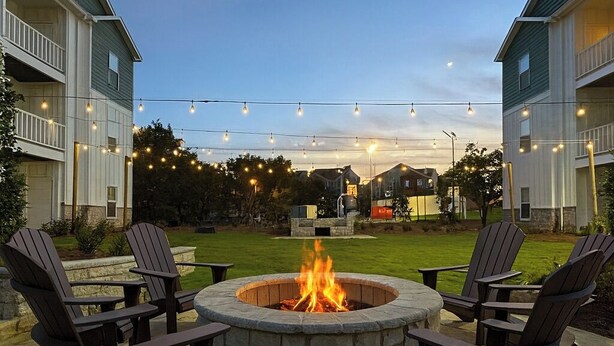 A fire pit with four Adirondack chairs in a courtyard, surrounded by two-story buildings with balconies. - Walk to Davis Wade Stadium, Pet Friendly, King Bed (Starkville)
