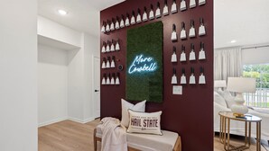 A room with a wall-mounted light fixture, a neon sign, a bench with a cushion, and a small table with a lamp. - Walk to Davis Wade Stadium, Pet Friendly, King Bed (Starkville)