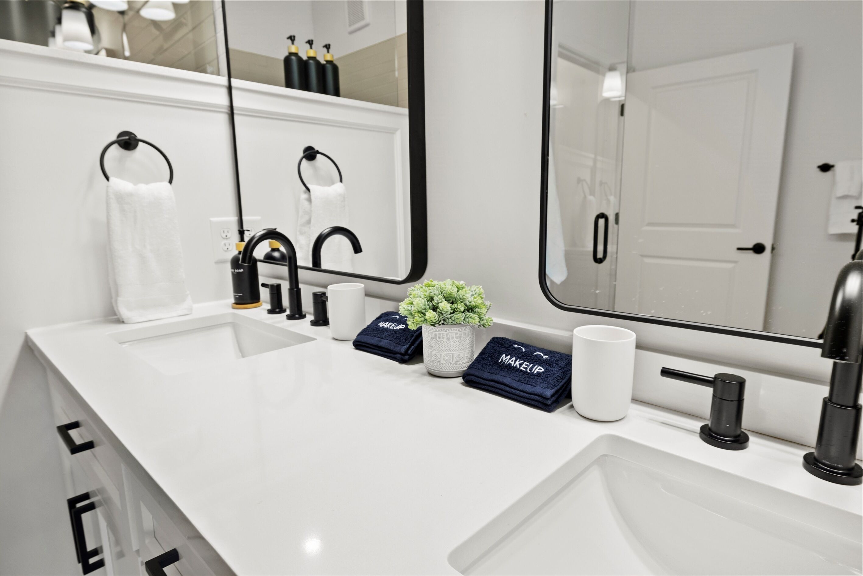 Une salle de bain moderne avec un lavabo blanc, des robinets noirs, un grand miroir et une plante en pot.