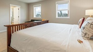 A bedroom with a large bed, a wooden headboard, two windows, and a door leading to another room.