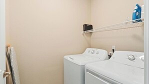 A laundry room with two white washing machines and a shelf with a blue iron and a black box.