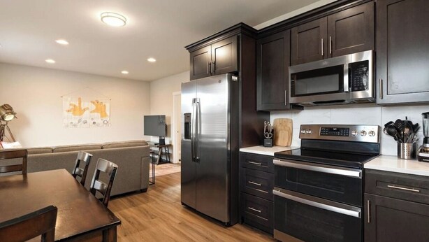 A modern kitchen with dark cabinetry, stainless steel appliances, and a wooden dining table.