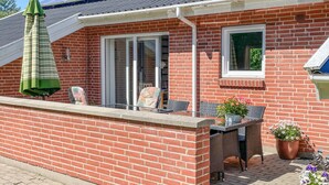 Una casa de maó amb un pati que té taula i cadires, un parasol verd i plantes en testos.