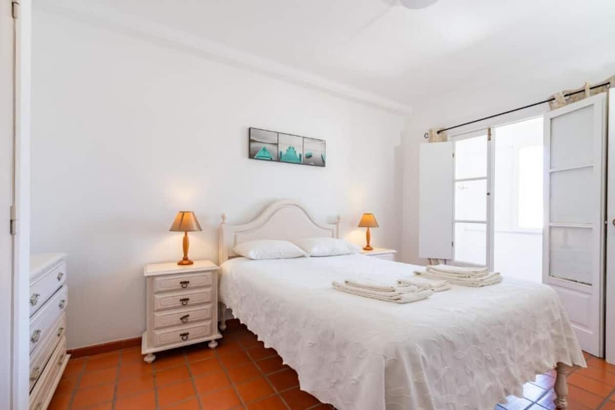 Ein Schlafzimmer mit einem Bett, Nachttischen, einer Kommode und einer Tür.