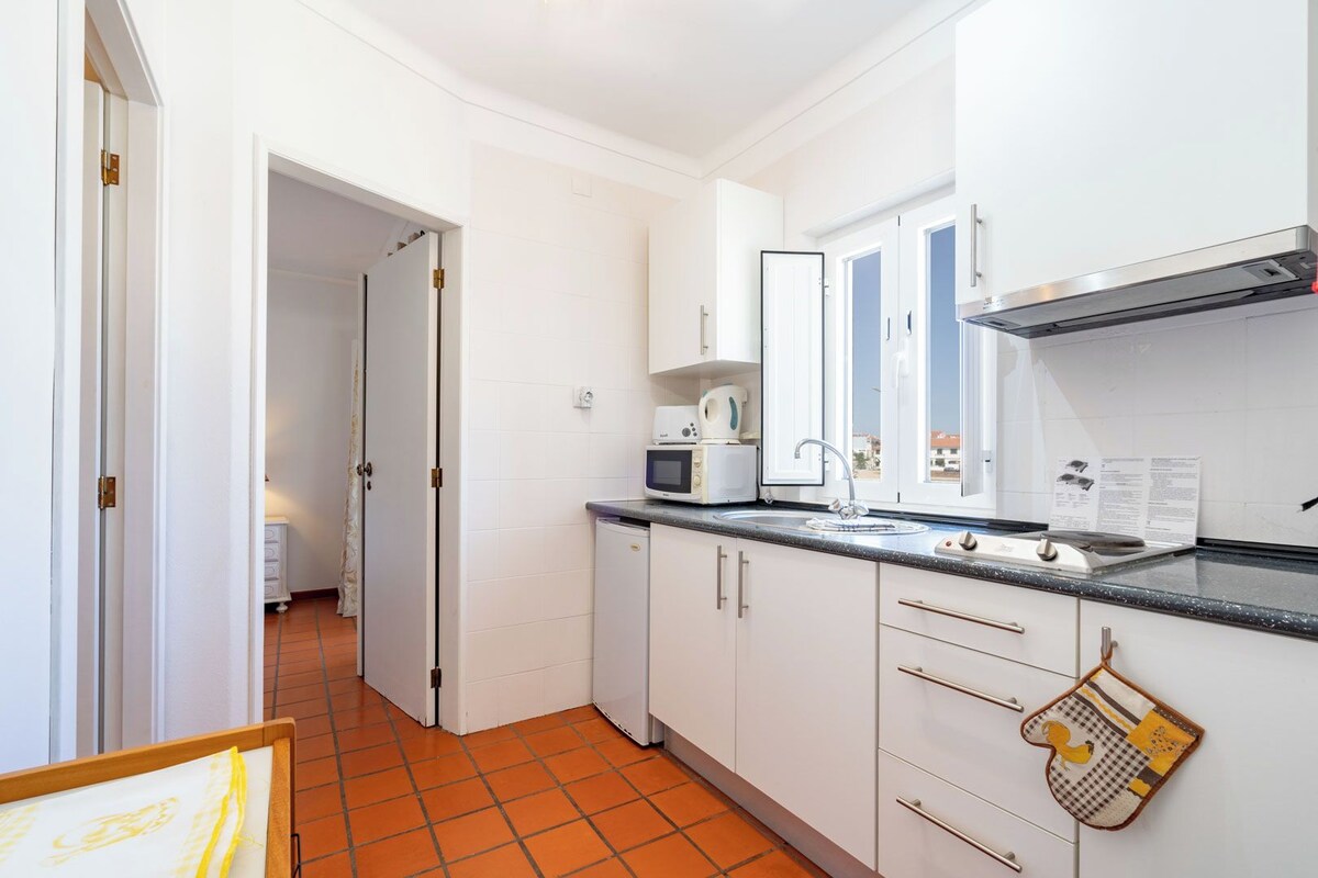 Une cuisine de taille réduite avec des meubles blancs, un four à micro-ondes, un évier et une cuisinière.