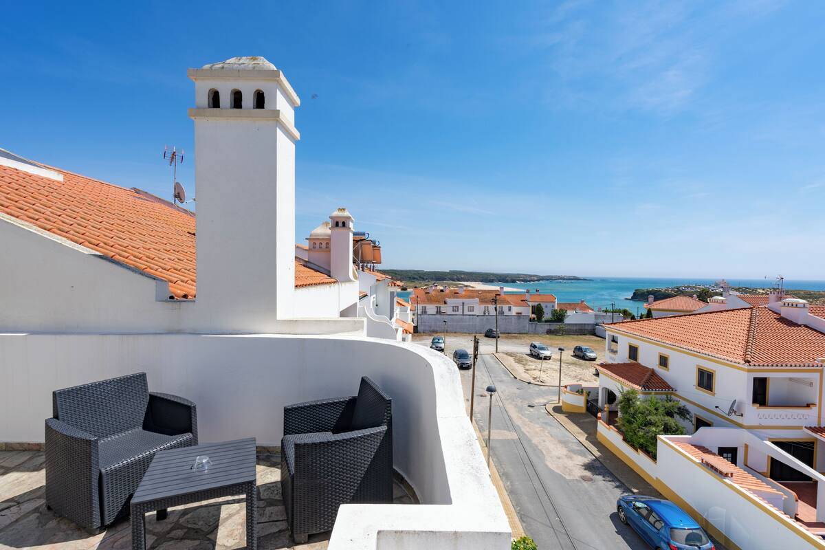 Eine Terrasse mit Korbmöbeln und freiem Blick auf das Meer und die darunterliegende Stadt.