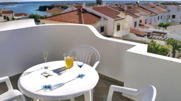 Een ronde tafel met stoelen op een balkon met uitzicht op een kustplaatsje met terracottedaken.