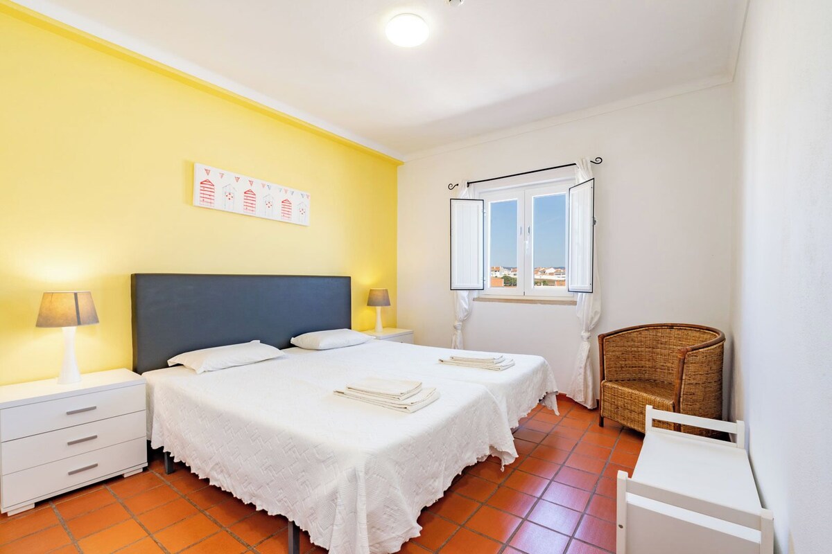 Une chambre d’hôtel avec deux lits, une fenêtre avec des rideaux, une chaise et une petite table.