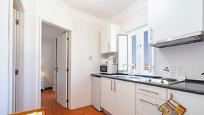 Une cuisine compacte avec des meubles blancs, un four à micro-ondes, un évier et un petit réfrigérateur.