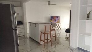 Een moderne keuken met een marmeren aanrecht, houten stoelen en een televisie op de achtergrond.