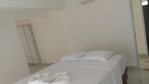 Een nette, minimalistische hotelkamer met een bed, een wit kussen en een witte handdoek op het hoofdeinde.