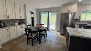 A modern kitchen with white cabinets, a stainless steel refrigerator, and a dining area with a checkered tablecloth.