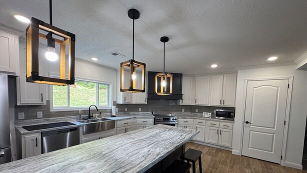 A modern kitchen with a marble countertop, stainless steel appliances, and pendant lighting.