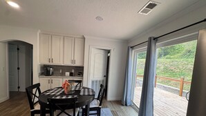 A modern kitchen with white cabinets, a dining table with checkered tablecloth, and a view of a wooden deck through large sliding glass doors.