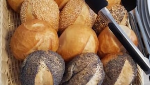 Un panier contenant un assortiment de pains et de petits pains, notamment des variétés aux graines de sésame et de pavot, posé sur un comptoir.