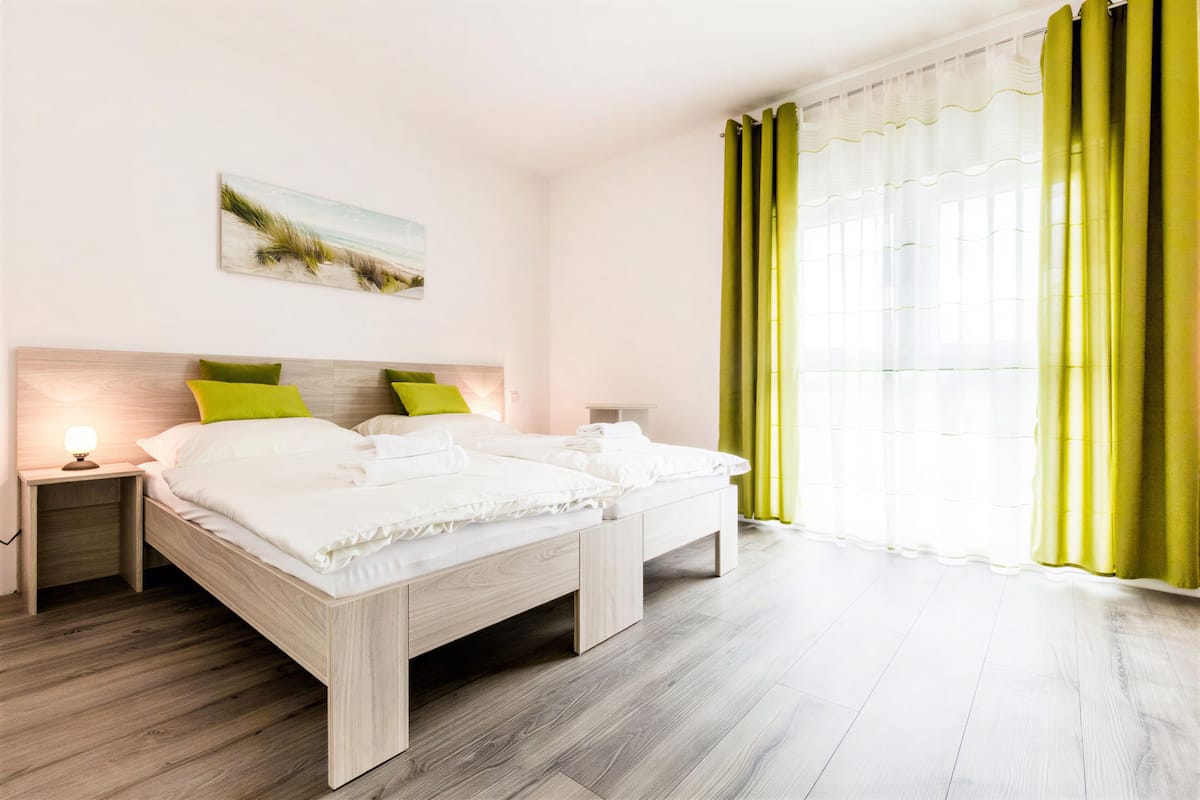A double bed with two pillows, a bedside table with a lamp, and a window with curtains.