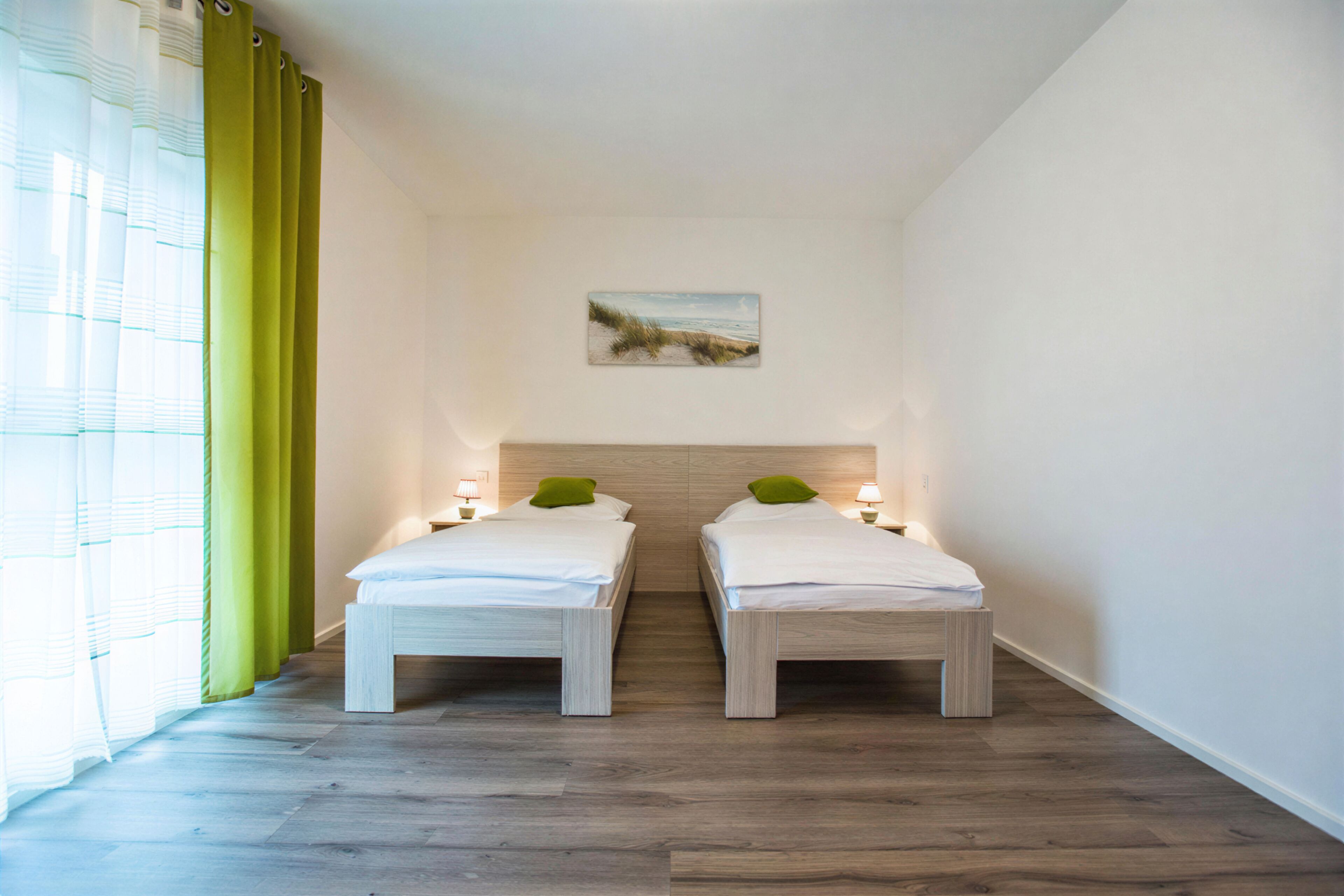 Een kamer met twee bedden, een schilderij aan de muur en een raam met gordijnen.
