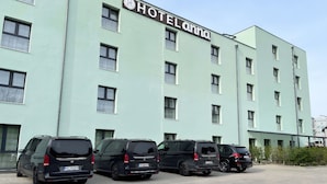 Un bâtiment d’hôtel avec une enseigne indiquant « HÔTEL ANNA ». Cinq voitures sont garées devant le bâtiment.